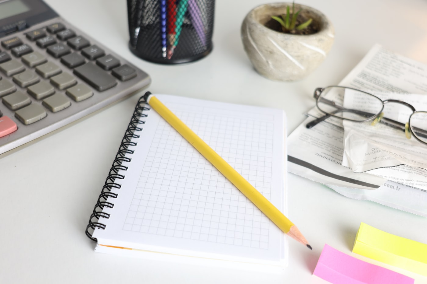 A desk with a calculator, a notebook, a pencil and reading glasses